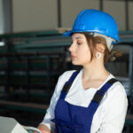 front view young attractive lady blue construction suit helmet controlling machines hangar working daytime buildings architecture construction